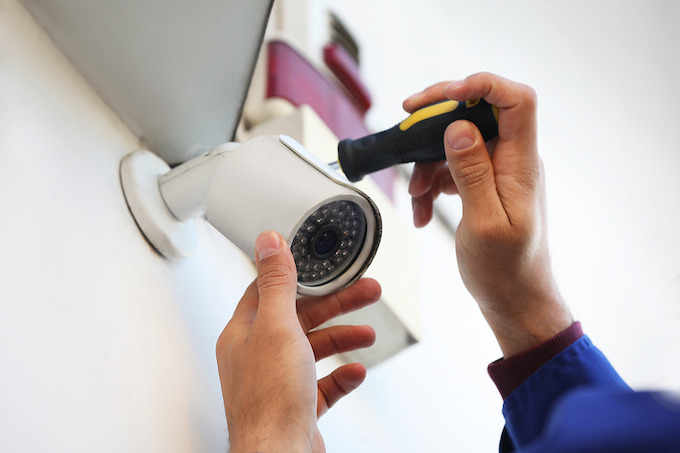 Technician installing CCTV camera on wall outdoors, closeup
